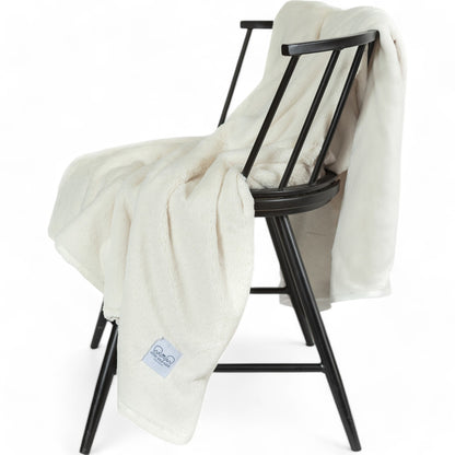 Luxury Borderless Throw Blanket in Ivory draped over a black chair, showcasing its soft and lightweight texture.